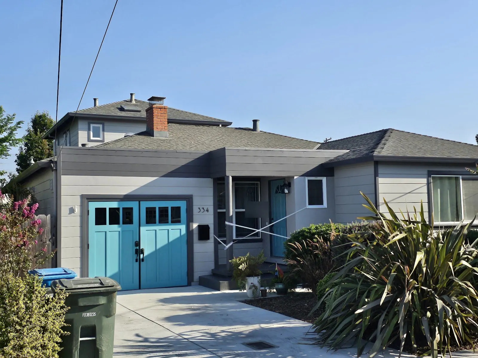 Single-story house repainted gray with teal carriage-style garage doors