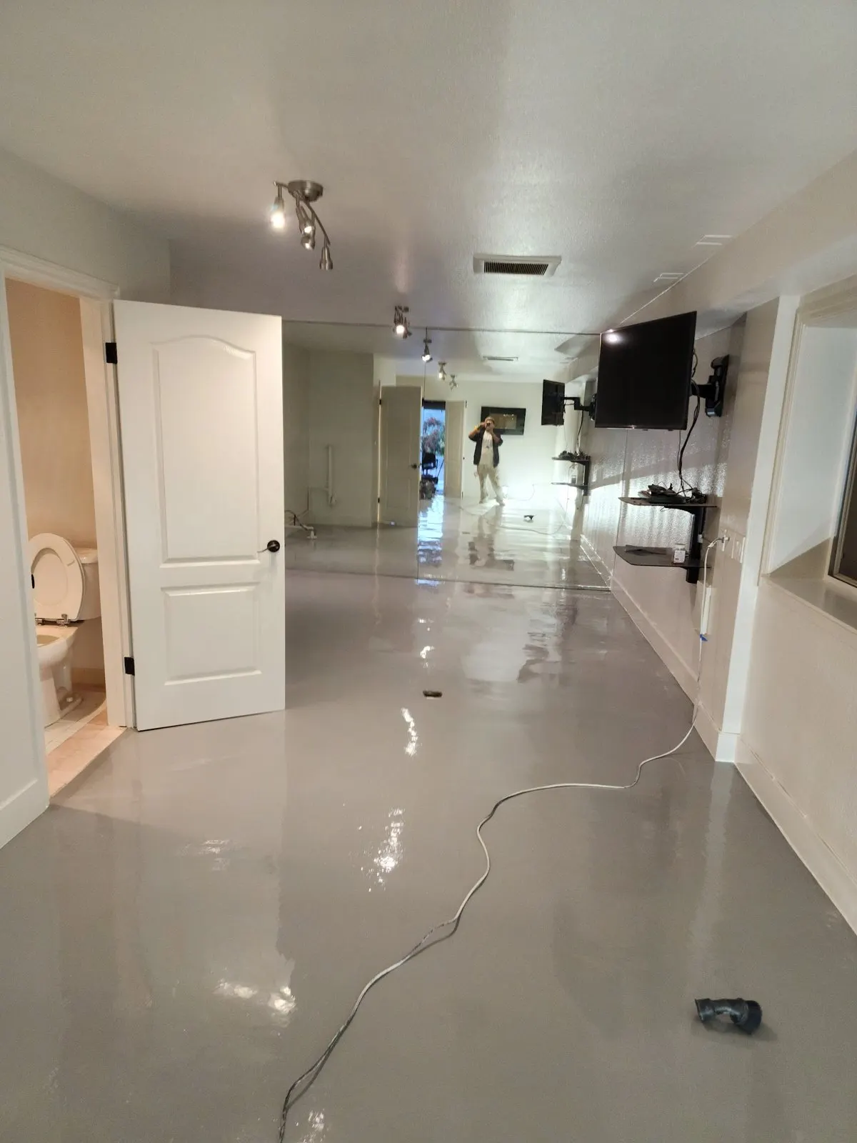 Long finished room with white walls, white doors and a glossy gray floor