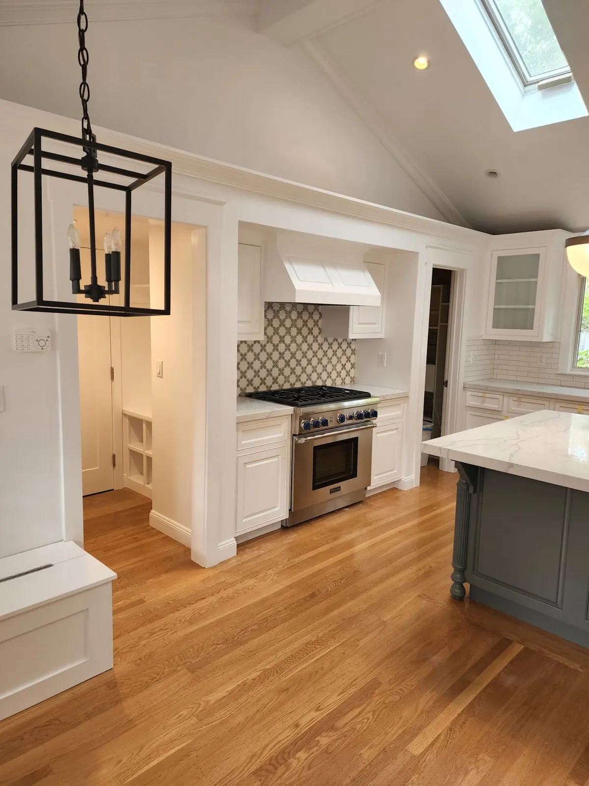 Kitchen with white painted cabinets, a gray island and a skylight